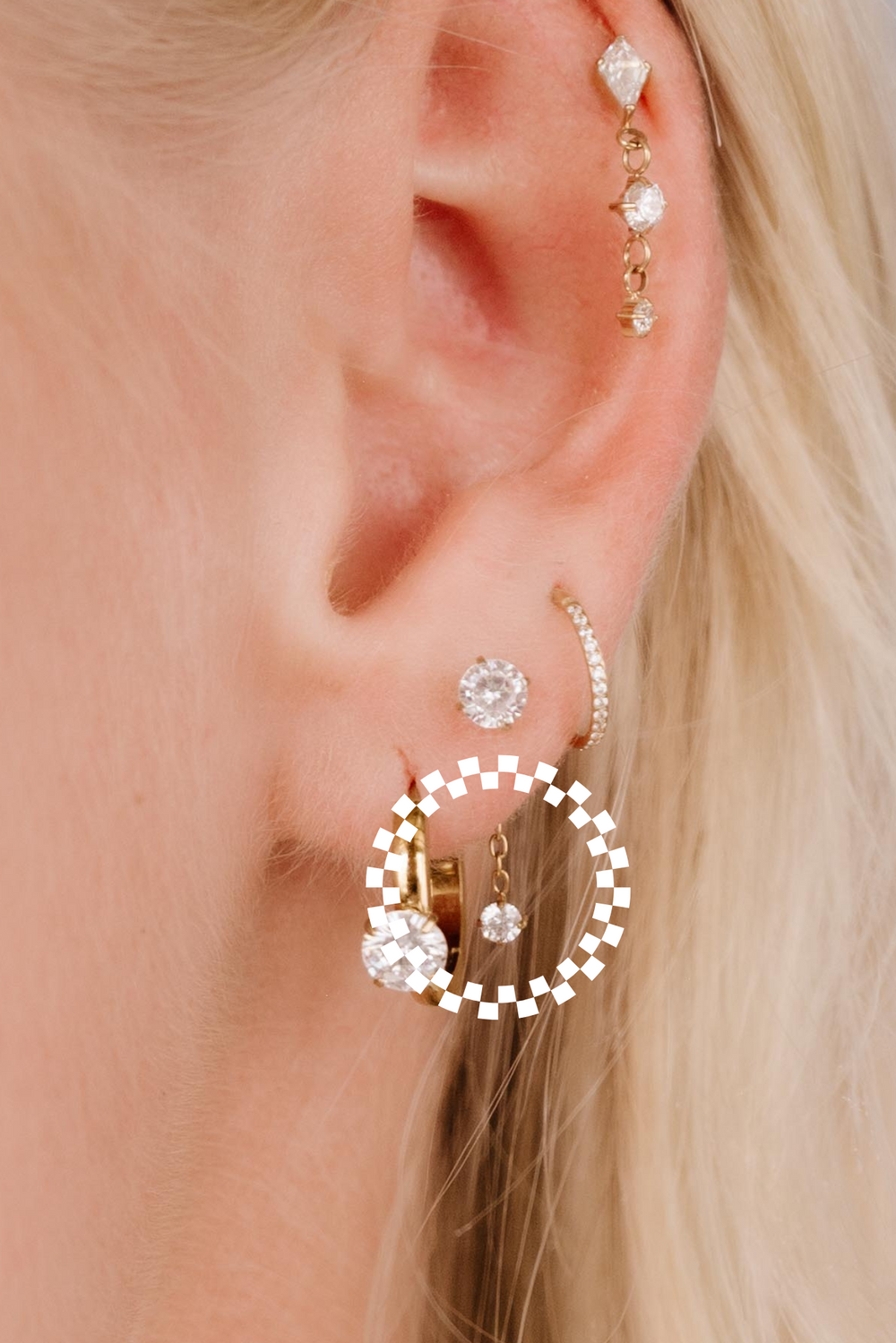 Close-up of an ear wearing gold hoop earrings with clear gemstones.