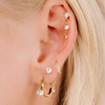 Close-up of an ear with multiple gold and diamond earrings against a blurred background