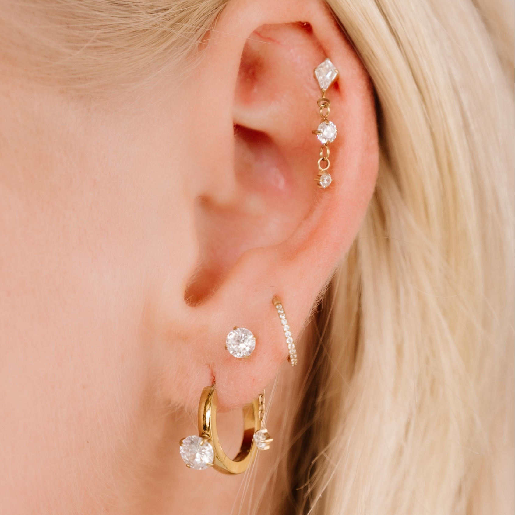 Close-up of an ear with multiple gold and diamond earrings against a blurred background