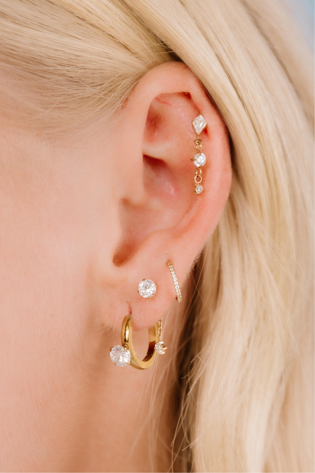 Close-up of an ear with multiple gold and diamond earrings against a blurred background