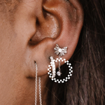 Close-up of an ear wearing a bow-shaped earring with a zirconia charm drop and other hoop earrings.