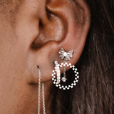 Close-up of an ear wearing a bow-shaped earring with a zirconia charm drop and other hoop earrings.