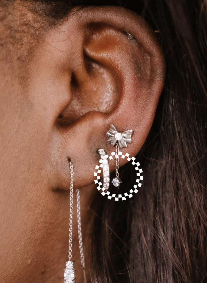 Close-up of an ear wearing a bow-shaped earring with a zirconia charm drop and other hoop earrings.