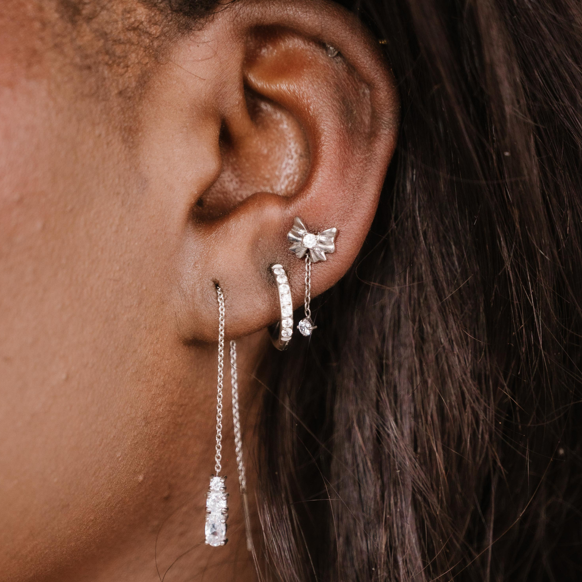 Close-up of an ear with silver earrings against a dark background