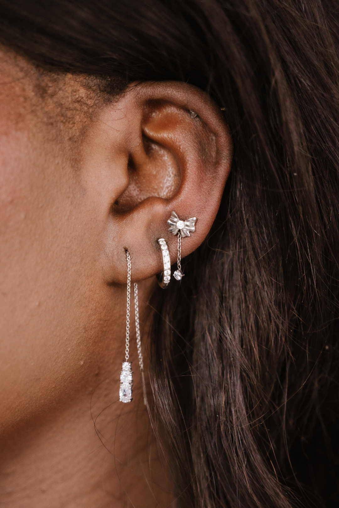 Close-up of an ear with silver earrings against a dark background