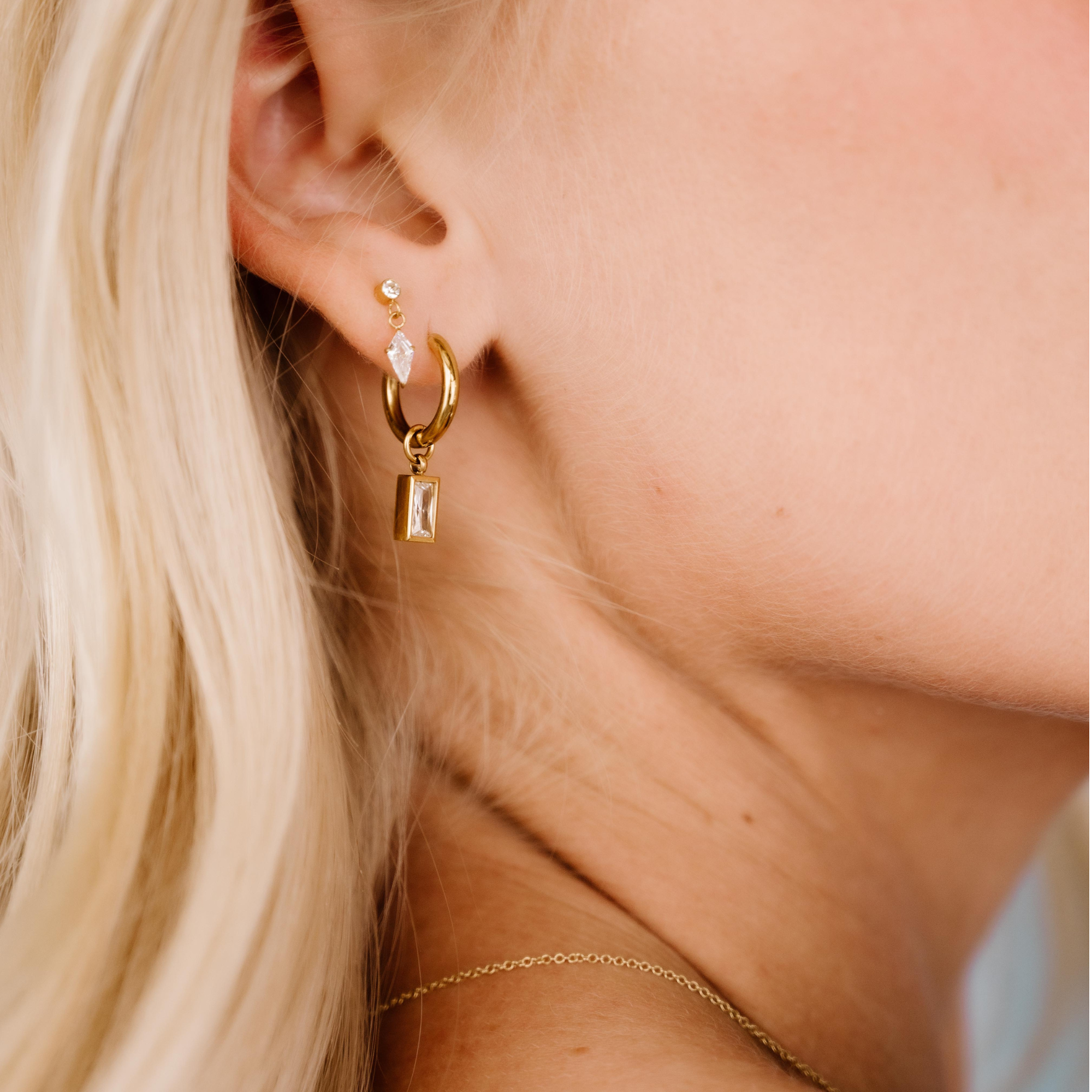 Close-up of a person wearing gold hoop earrings with small dangling charms.