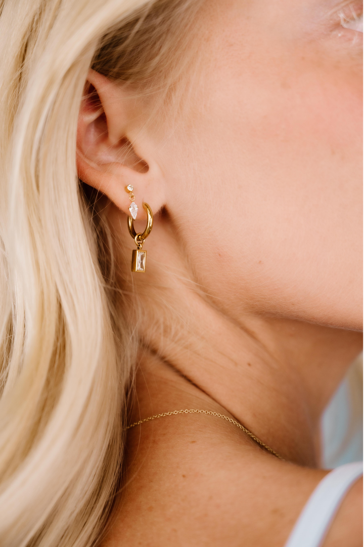 Close-up of a person wearing gold hoop earrings with small dangling charms.