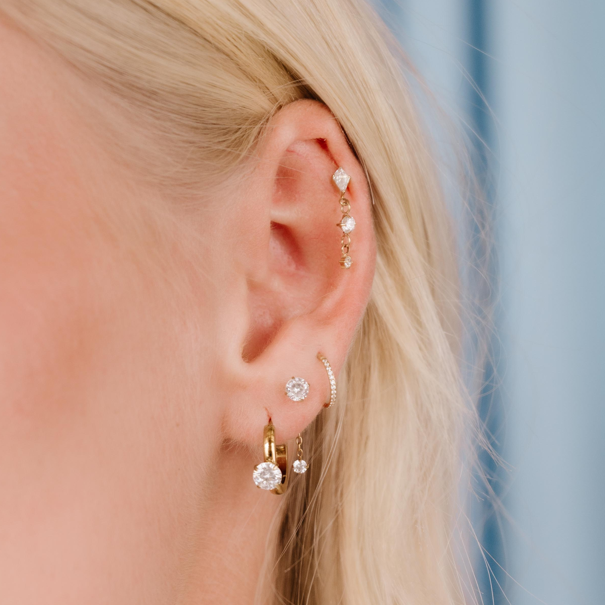 Close-up of a person wearing multiple gold earrings with clear gemstones against a blurred background.