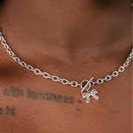 Silver chain necklace with a bow charm on a person's neck