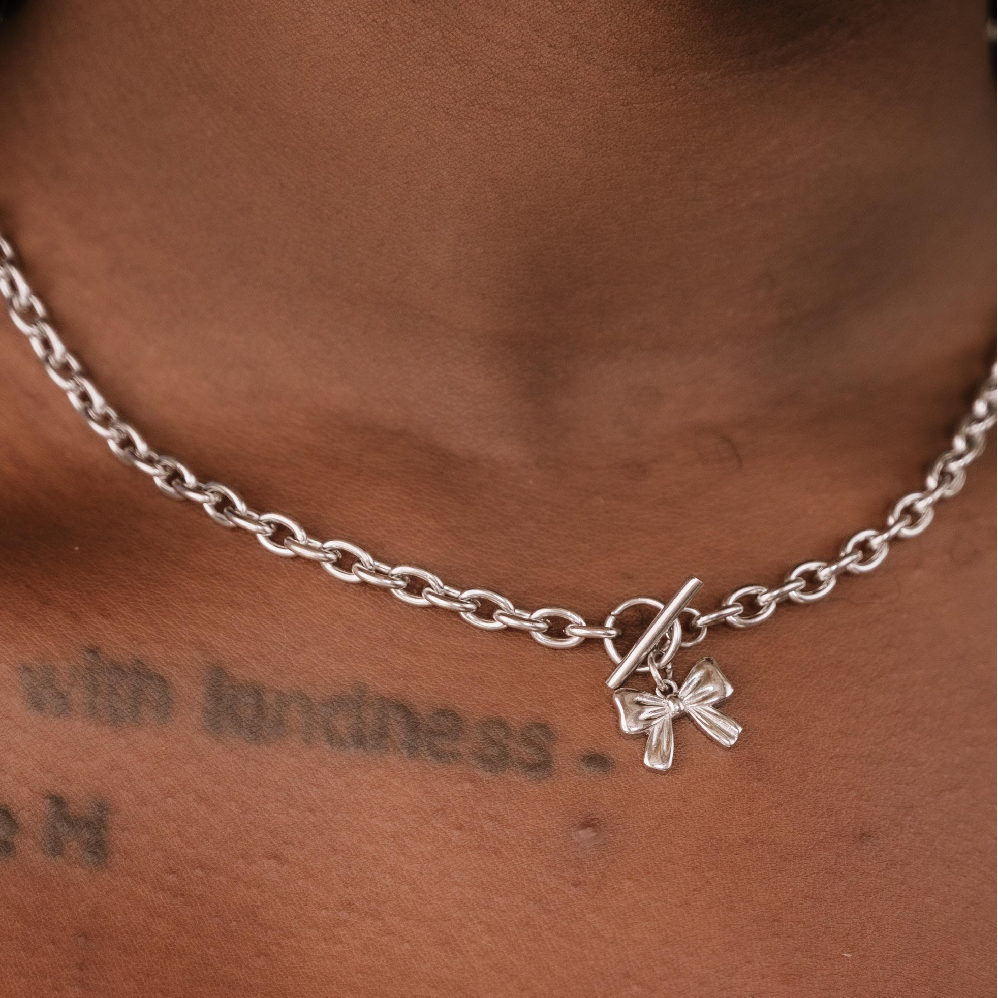 Silver chain necklace with a bow charm on a person's neck