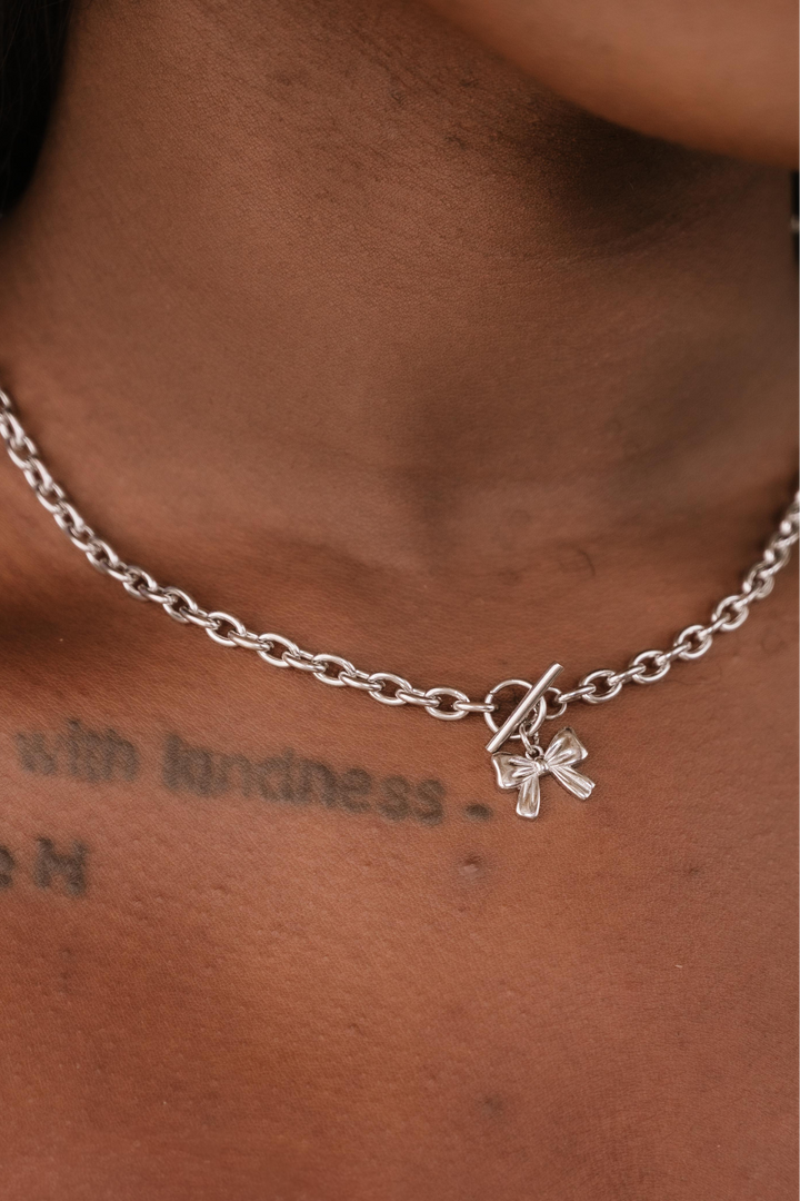 Silver chain necklace with a bow charm on a person's neck