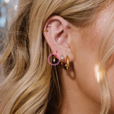 Close-up of a person wearing gold hoop earrings with pink and clear gemstones.