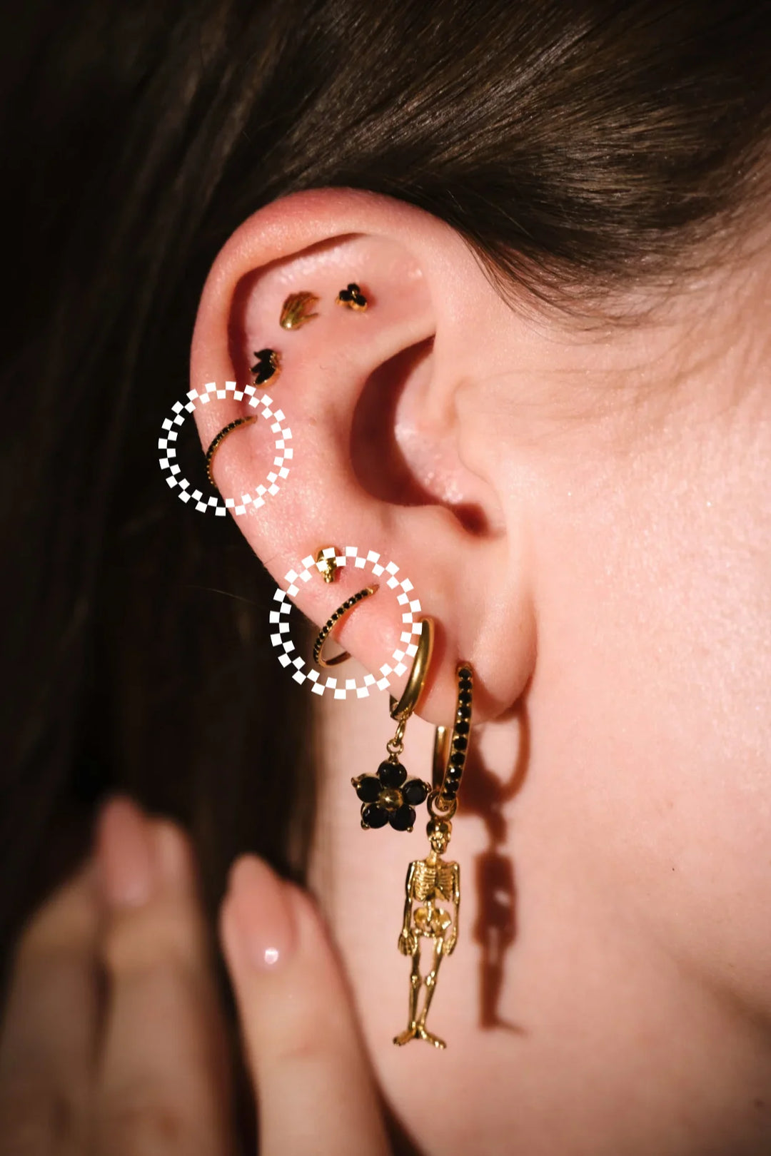 Close-up of an ear with gold earrings and a hand adjusting them.