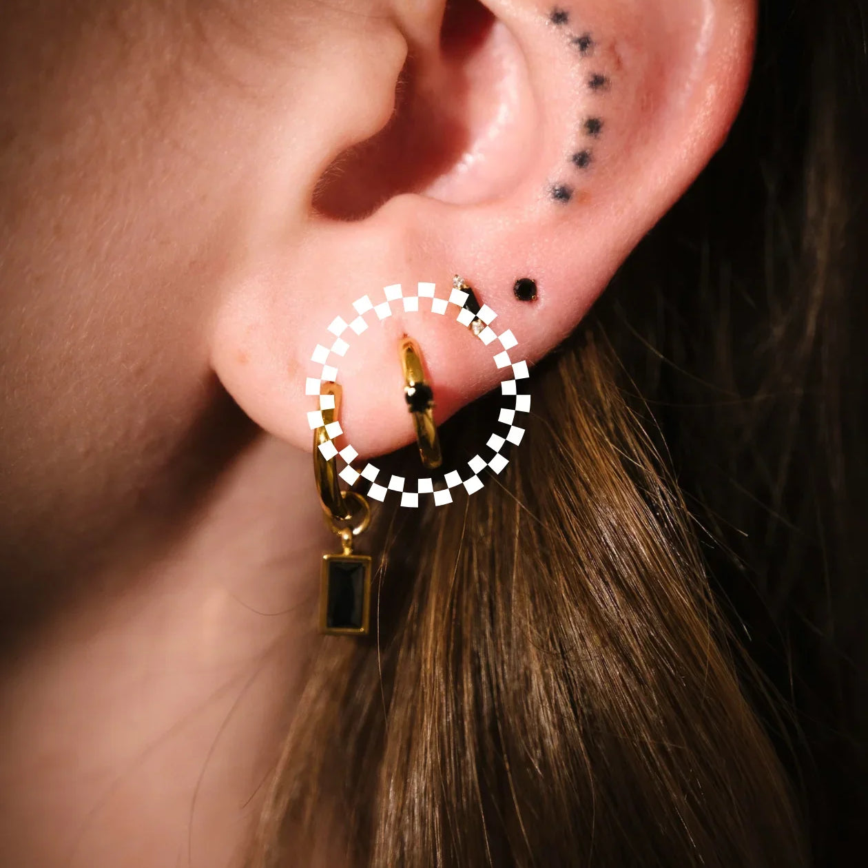 Close-up of an ear with a gold and black checkered hoop earring.