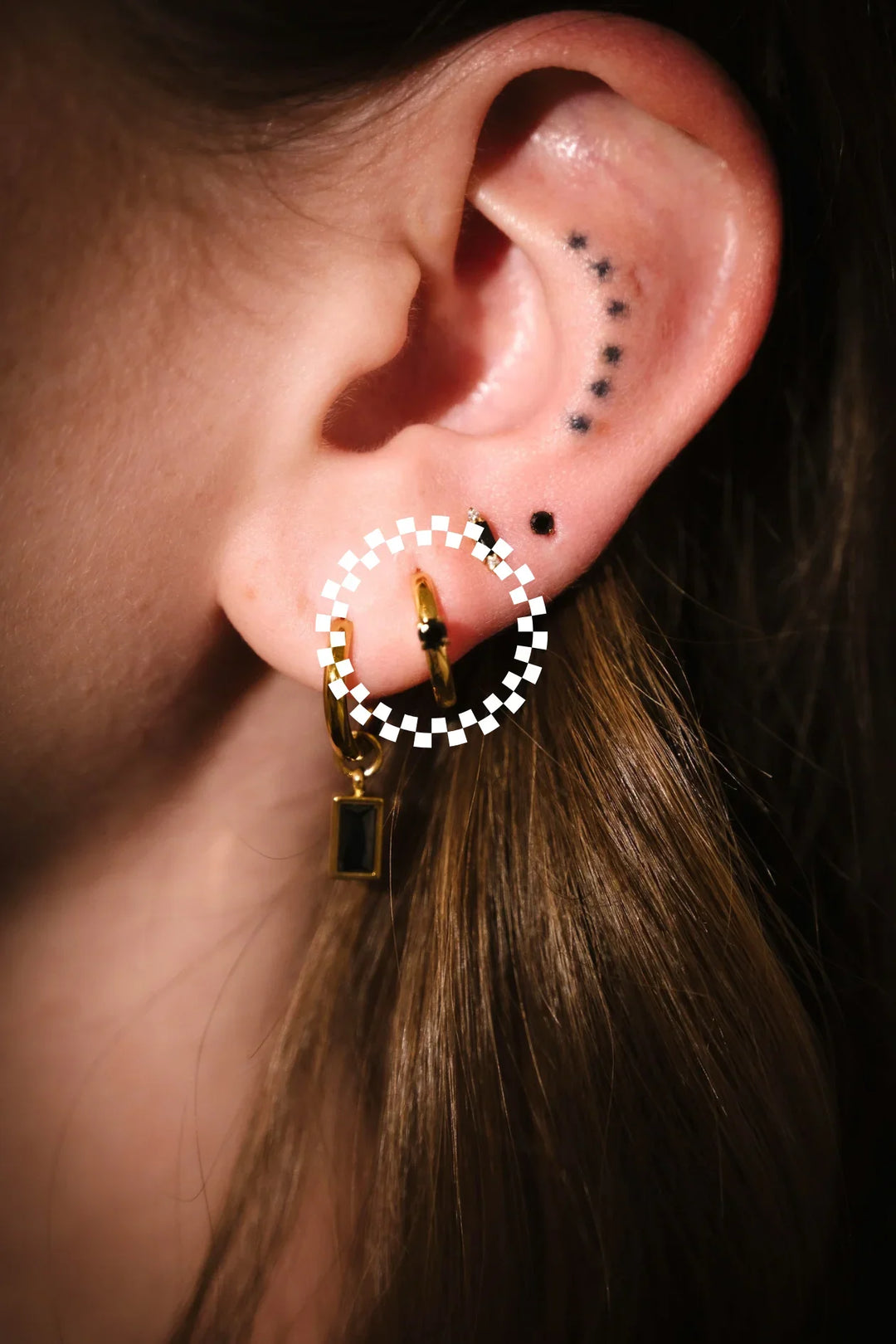 Close-up of an ear with a gold and black checkered hoop earring.