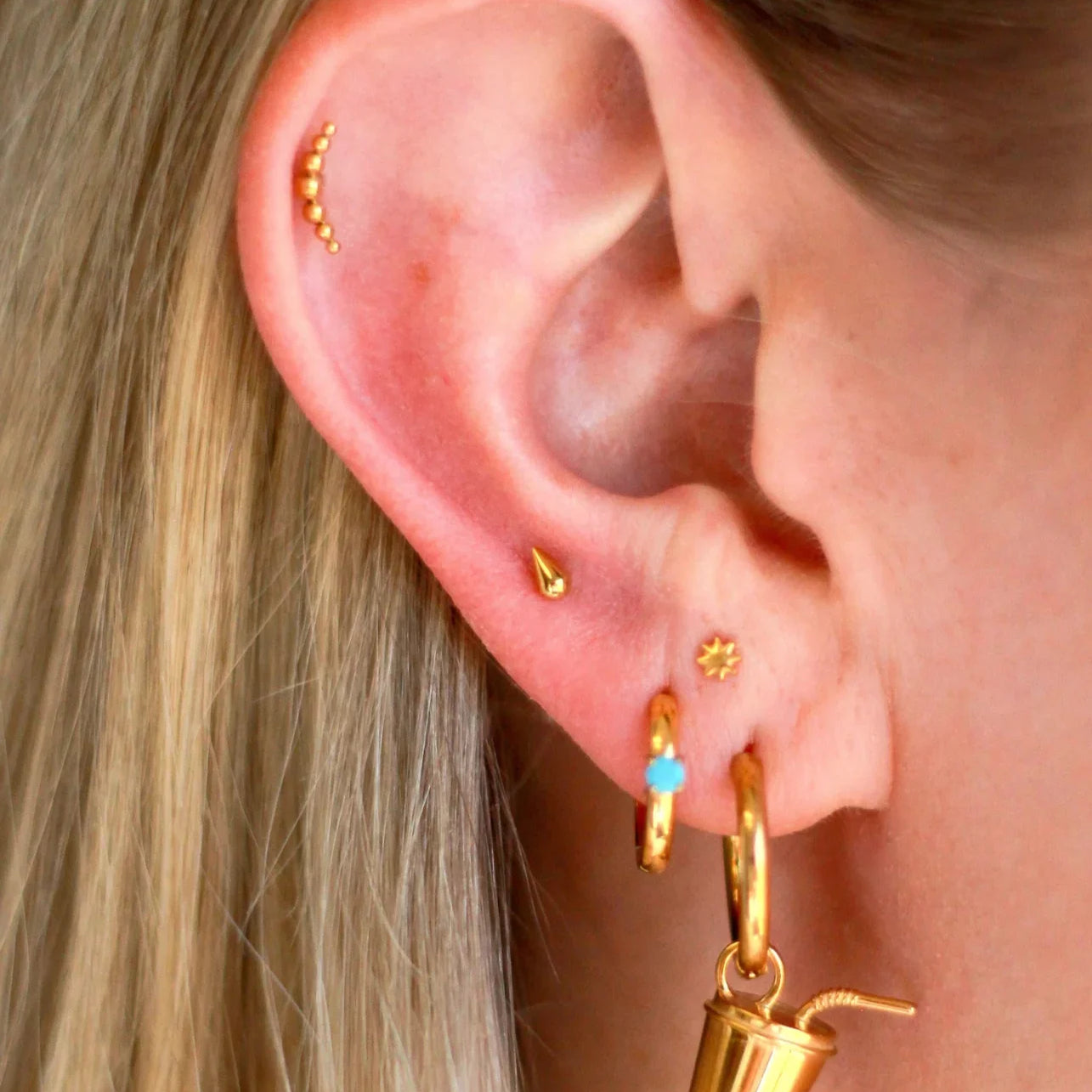 Close up of an ear with a lot of piercings, featuring gold flat backs studs and hoops
