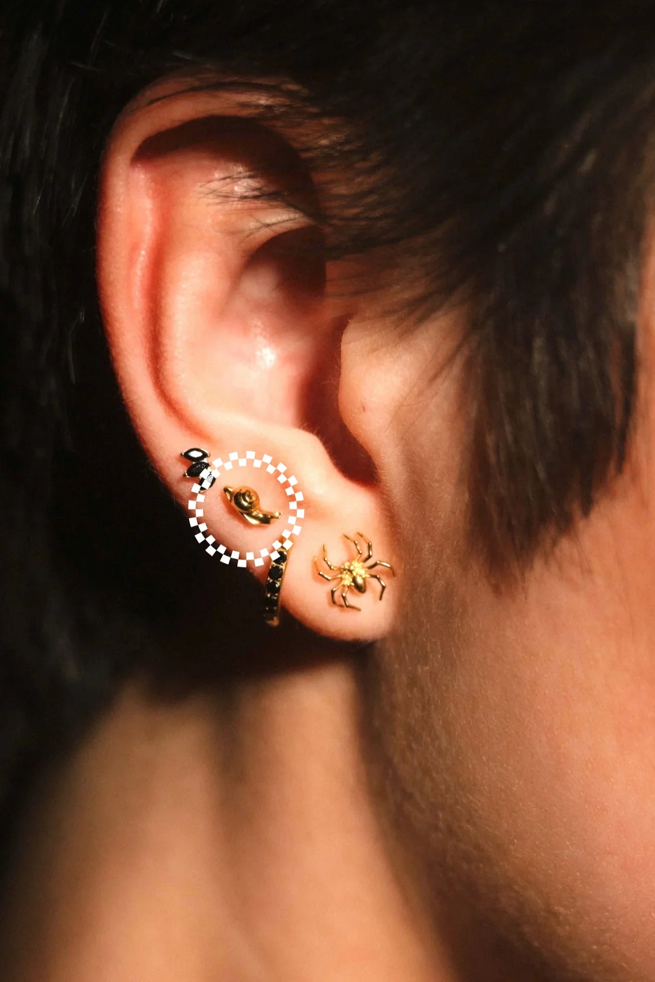 Close-up of an ear with multiple earrings, including a spider design.