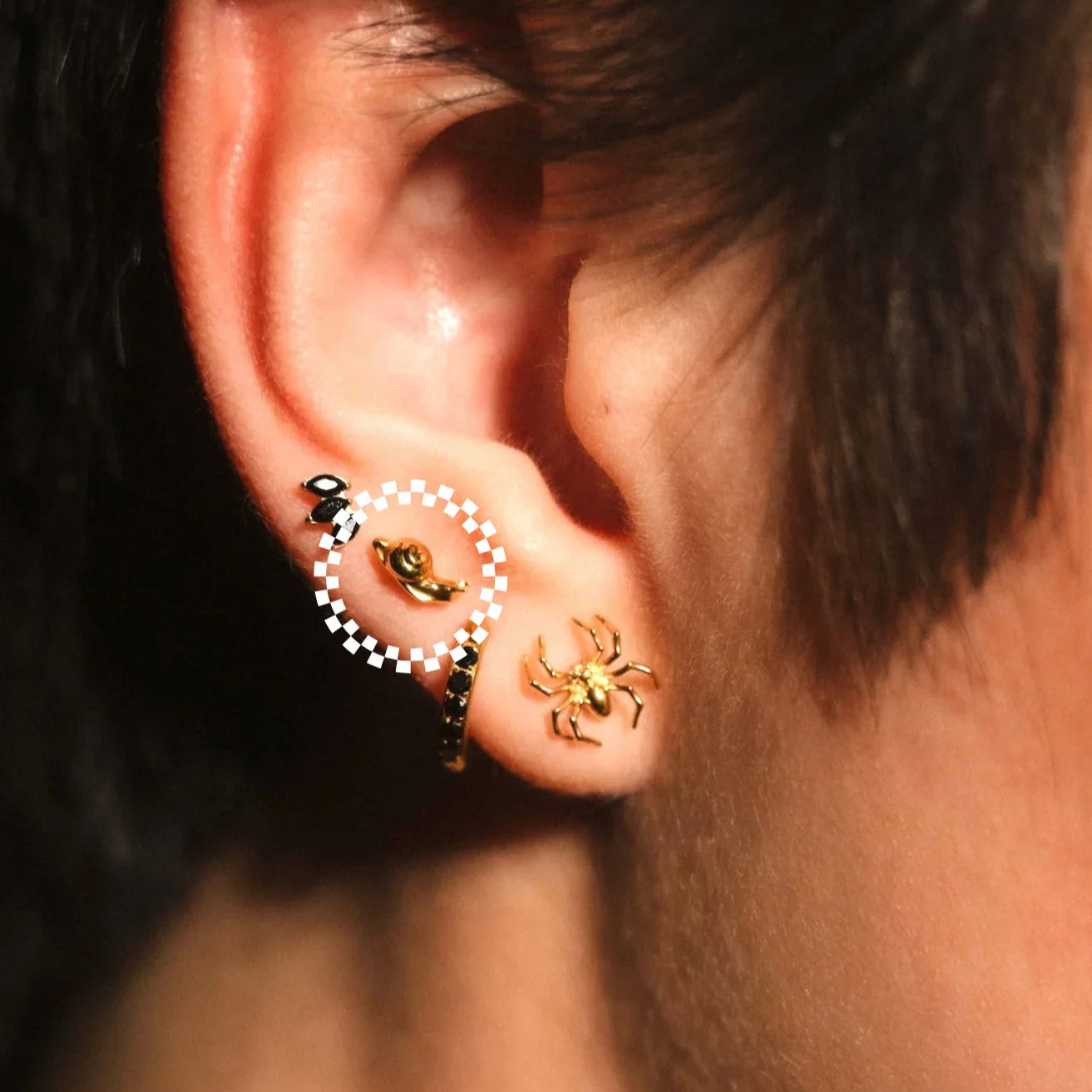 Close-up of an ear with multiple earrings, including a spider design.