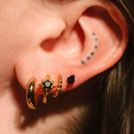 Close-up of an ear with gold hoop earrings and black studs.