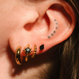 Close-up of an ear with gold hoop earrings and black studs.