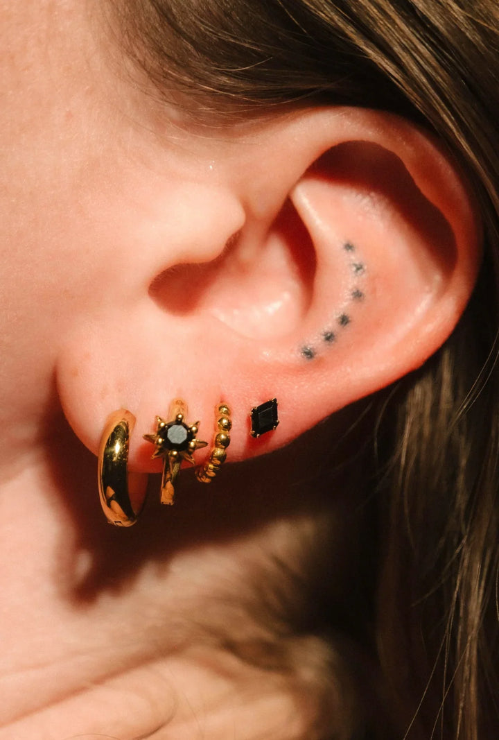Close-up of an ear with gold hoop earrings and black studs.