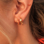 Close-up of an ear wearing gold hoop earrings with a blurred background