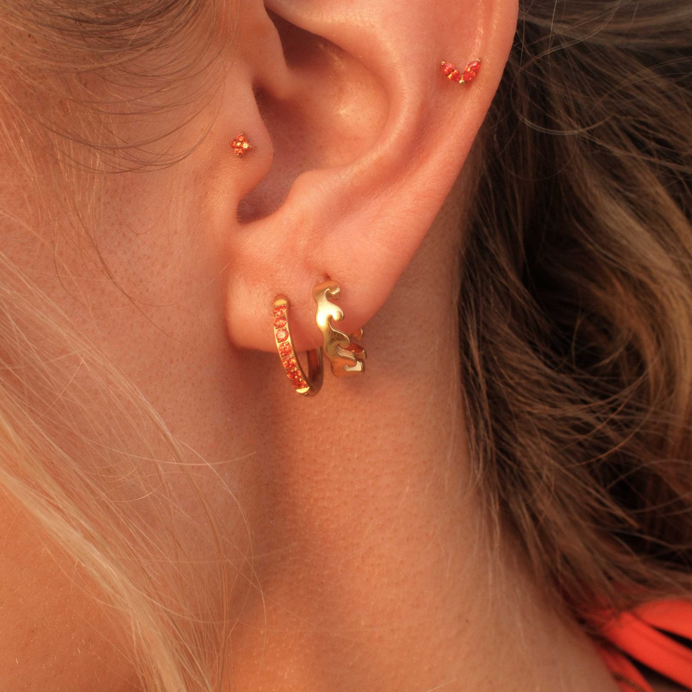 Close-up of an ear wearing gold hoop earrings with a blurred background