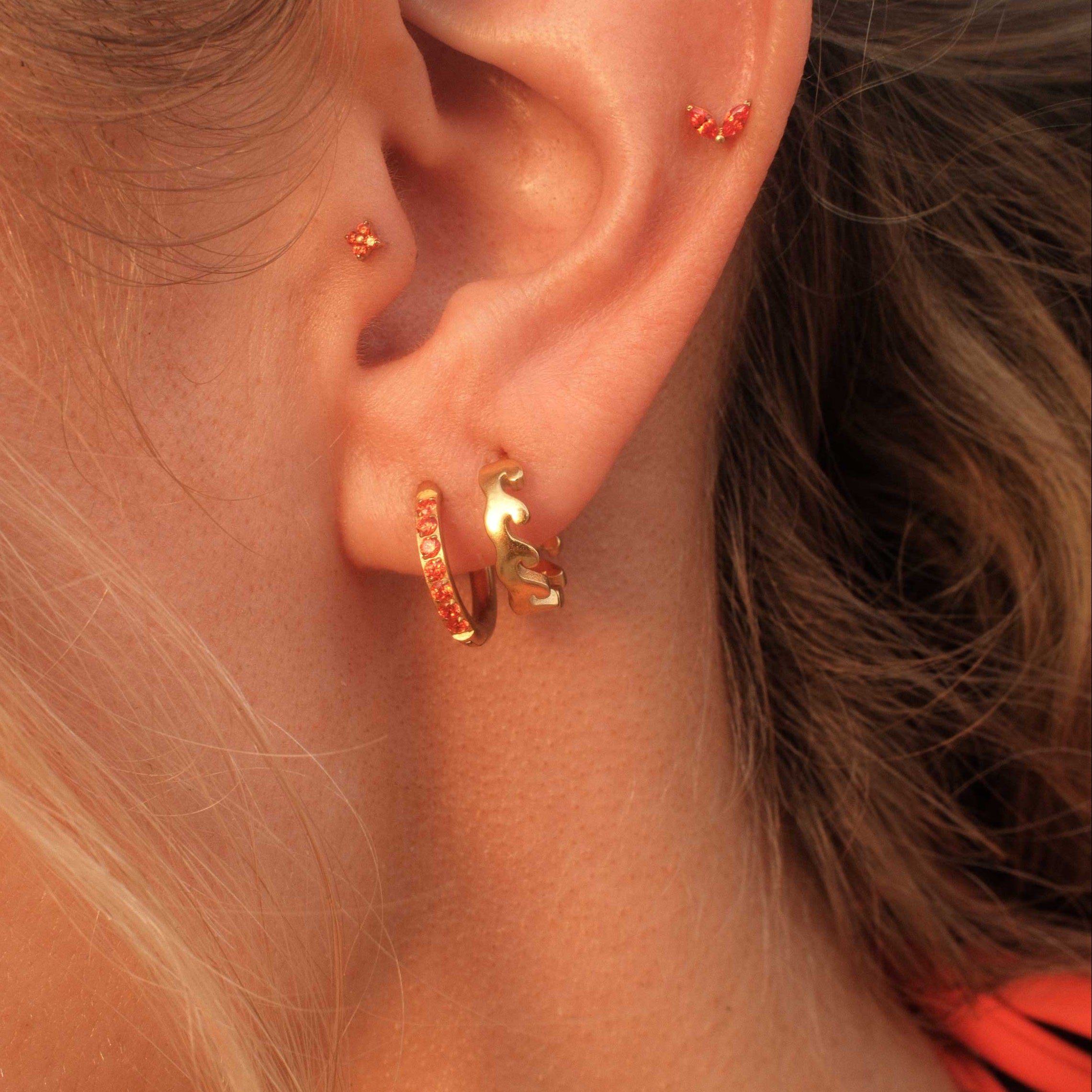 Close-up of an ear wearing gold hoop earrings with a blurred background