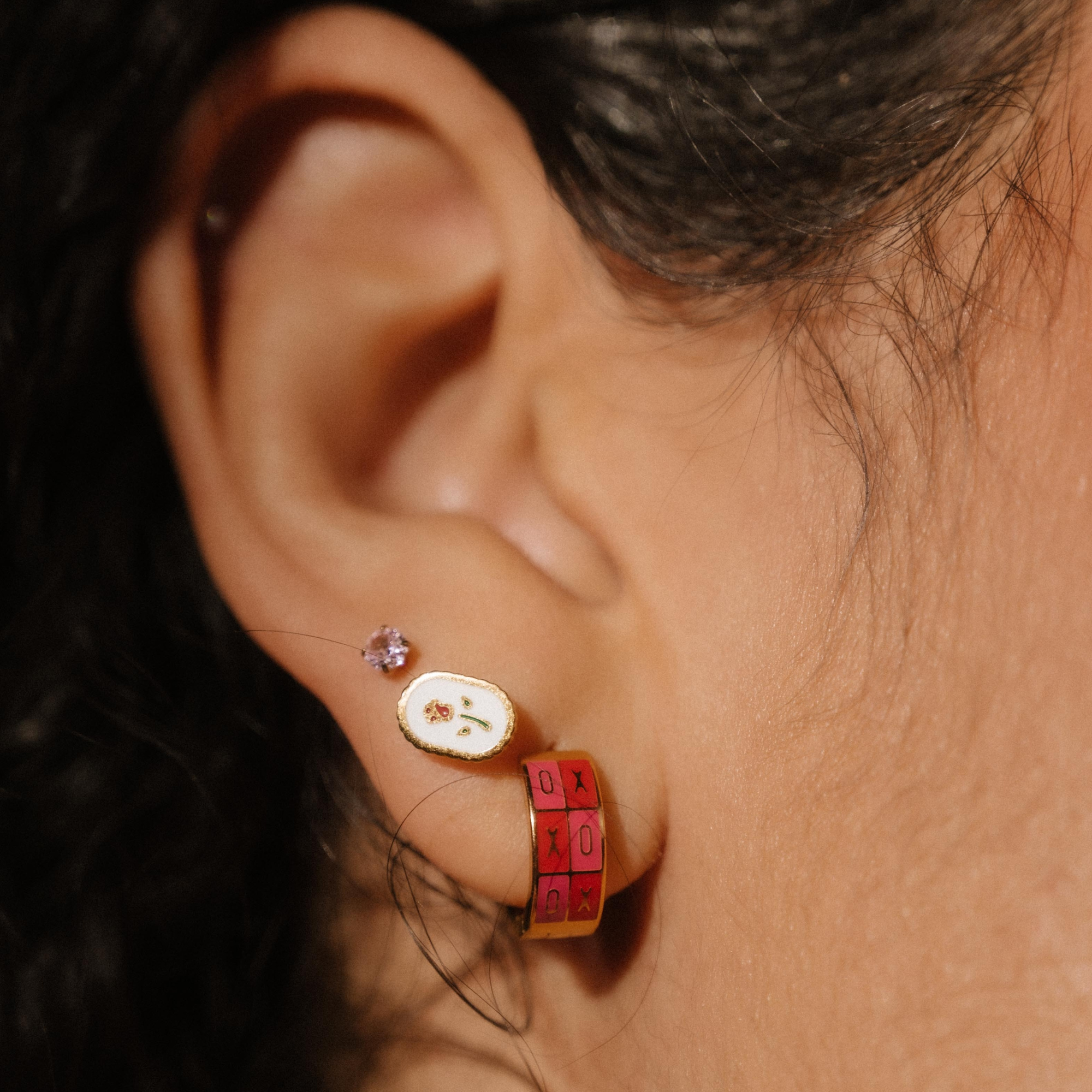 Close-up of an ear wearing a small earring with a red and gold design.