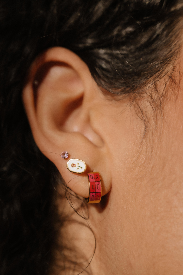 Close-up of an ear wearing a small earring with a red and gold design.