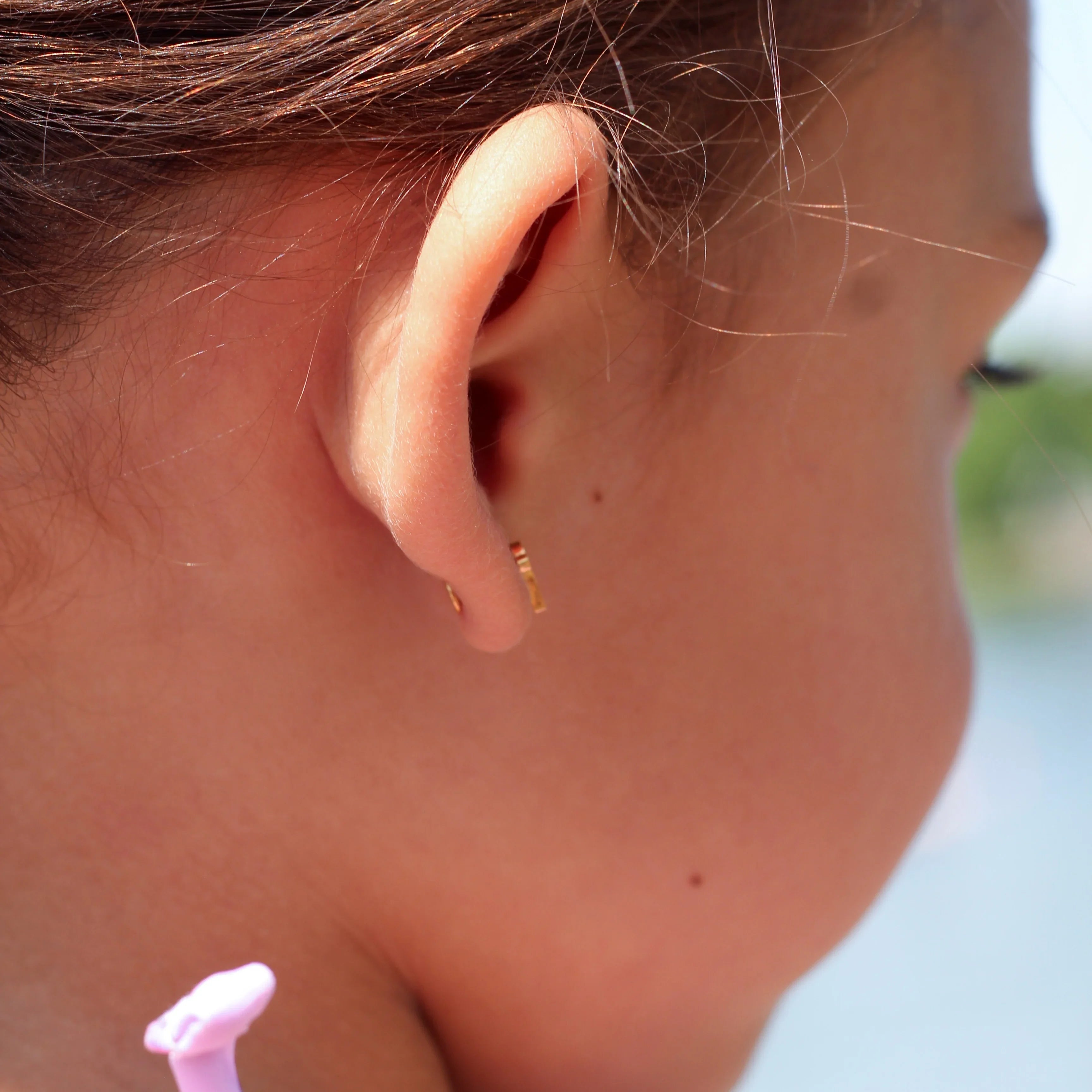 Close-up of a child's ear with a side view of a flat back earring, hair clip, and pink hair tie.