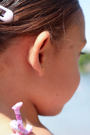 Close-up of a child's ear with a side view of a flat back earring, hair clip, and pink hair tie.