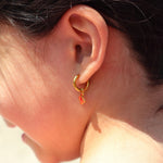 Close-up of an ear wearing a gold hoop earring with red crab charm on it.