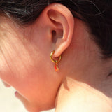 Close-up of an ear wearing a gold hoop earring with red crab charm on it.