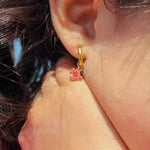Close-up of an ear wearing a gold hoop earring with red crab charm on it.