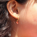 Close-up of an ear wearing a gold hoop earring with red crab charm on it.
