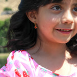 Young girl wearing a gold hoop with red crab charm on it and a pink shirt with strawberry pattern, outdoors