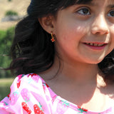 Young girl wearing a gold hoop with red crab charm on it and a pink shirt with strawberry pattern, outdoors