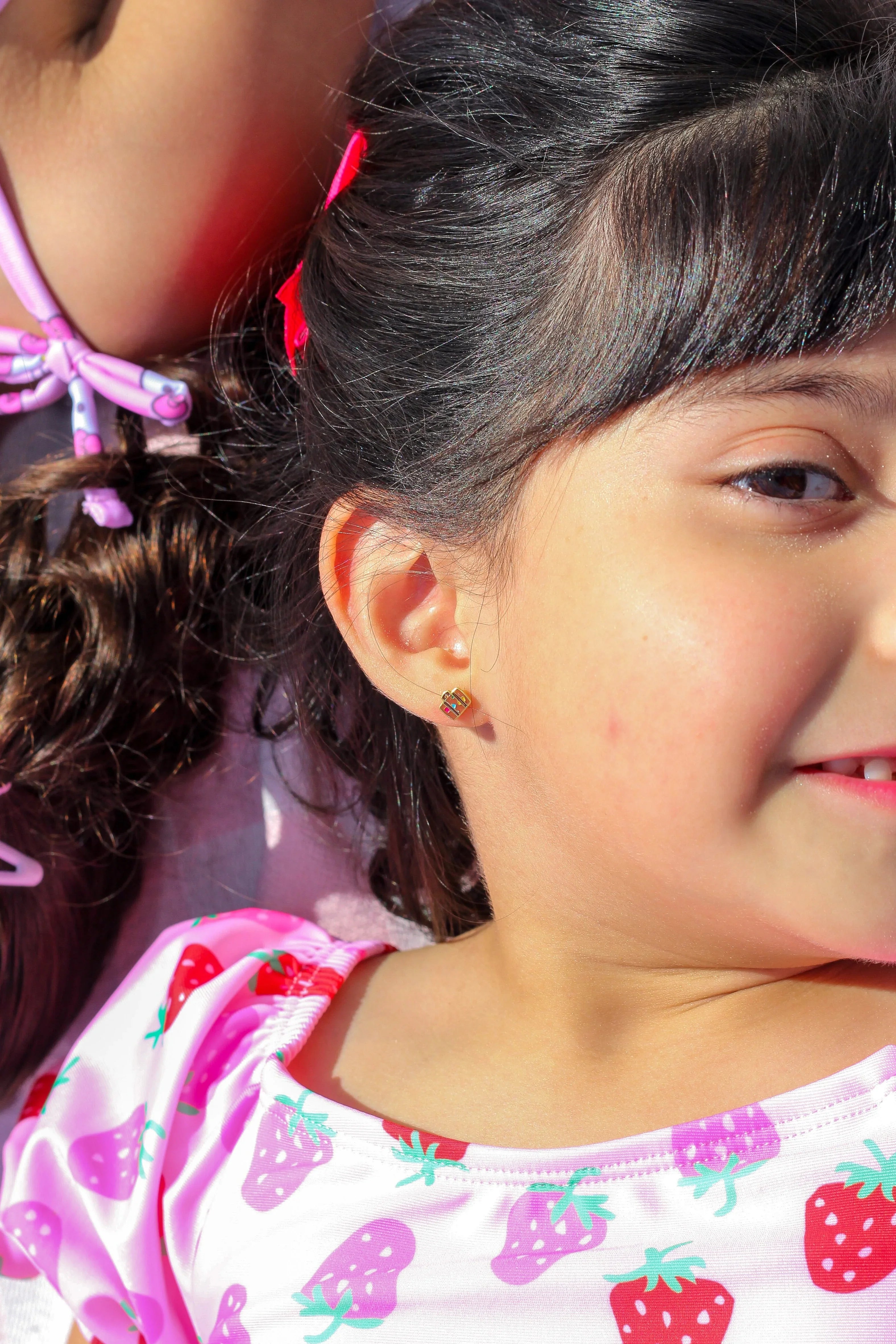 Close-up of a girl wearing a brown suitcase flat back stud earring, wearing a pink swimsuit with strawberry pattern.