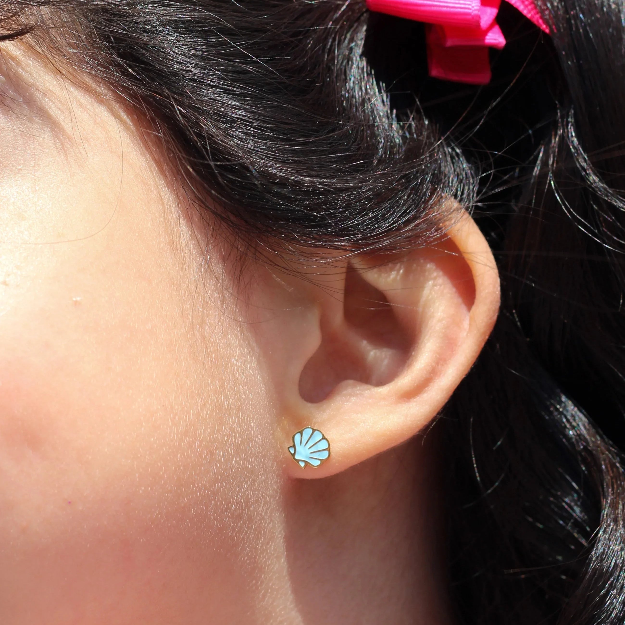 Close-up of an ear with a blue shell earring and hair with pink bows against a blue background