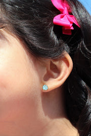 Close-up of an ear with a blue shell earring and hair with pink bows against a blue background