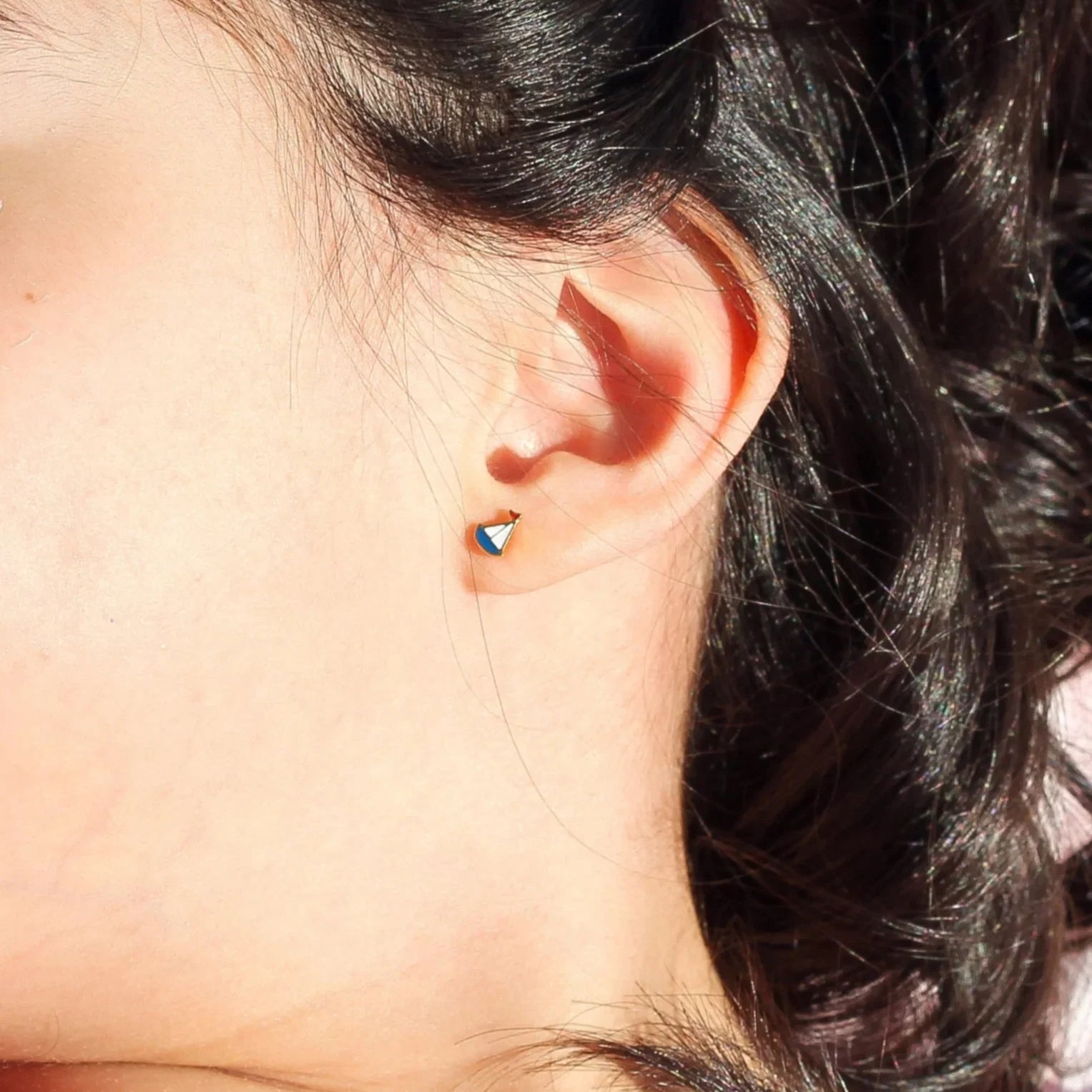 Girl with a pink bow in her hair wearing a sailboat earring and a pink shirt with strawberry pattern.