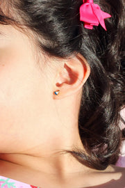 Girl with a pink bow in her hair wearing a sailboat earring and a pink shirt with strawberry pattern.