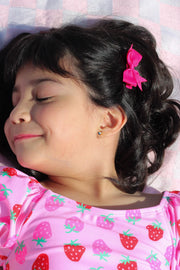Young girl with a pink bow in her hair, wearing a pink shirt with strawberry pattern, lying on a checkered blanket.