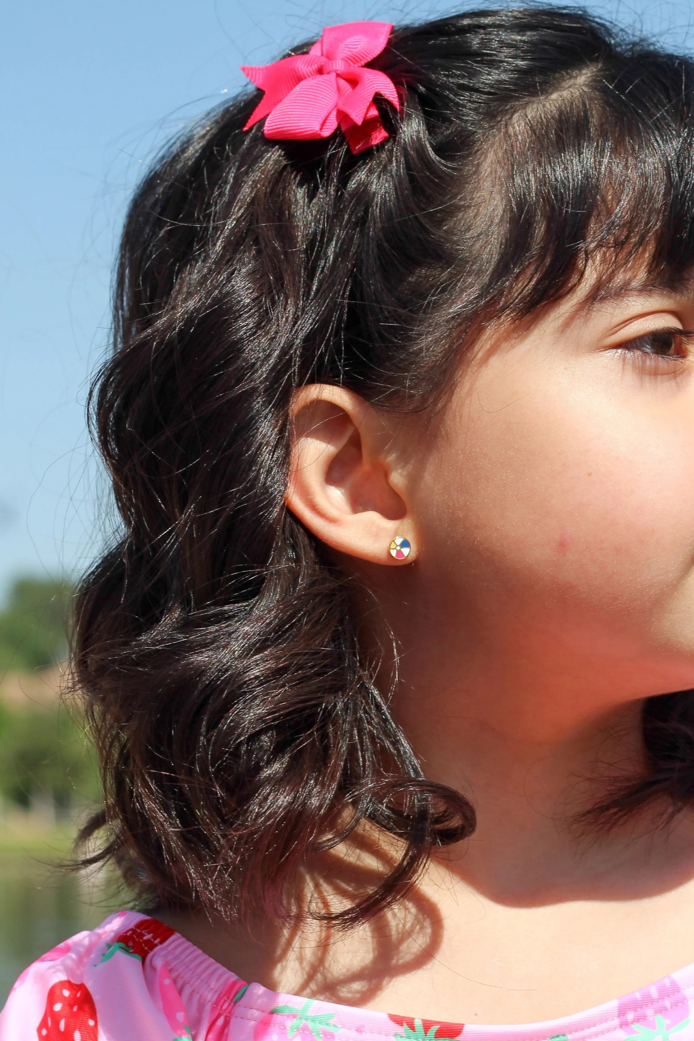 Girl wearing a beach ball stud earring and a pink shirt with strawberry pattern outdoors