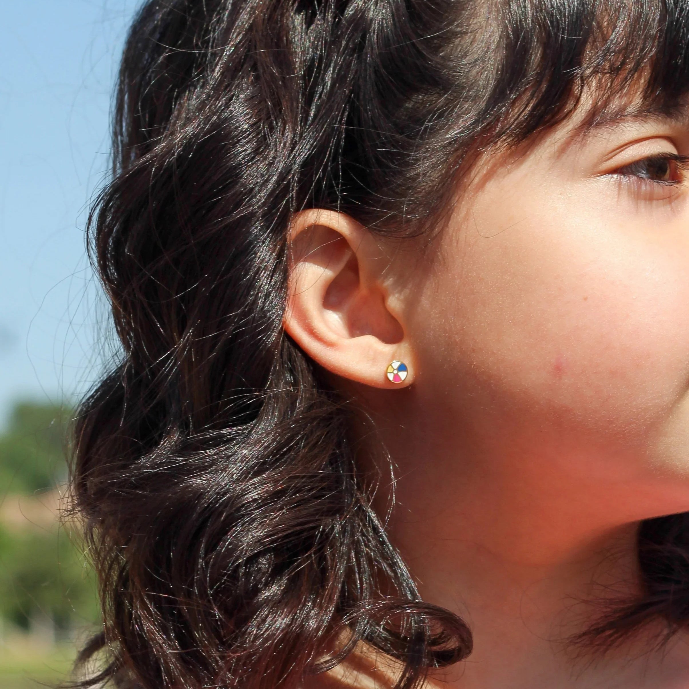 Girl wearing a beach ball stud earring and a pink shirt with strawberry pattern outdoors