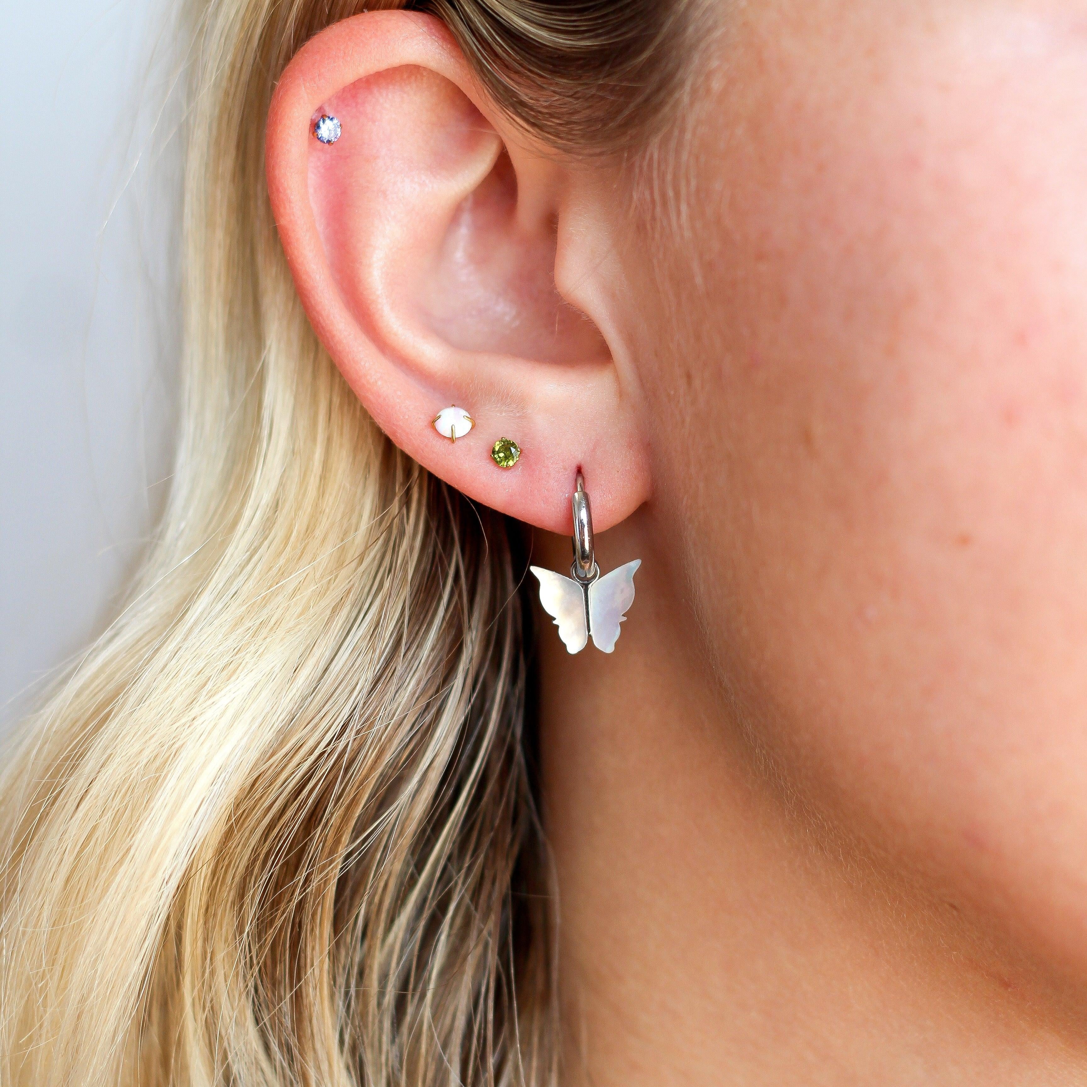Close-up of a person wearing butterfly-shaped earrings with a plain background