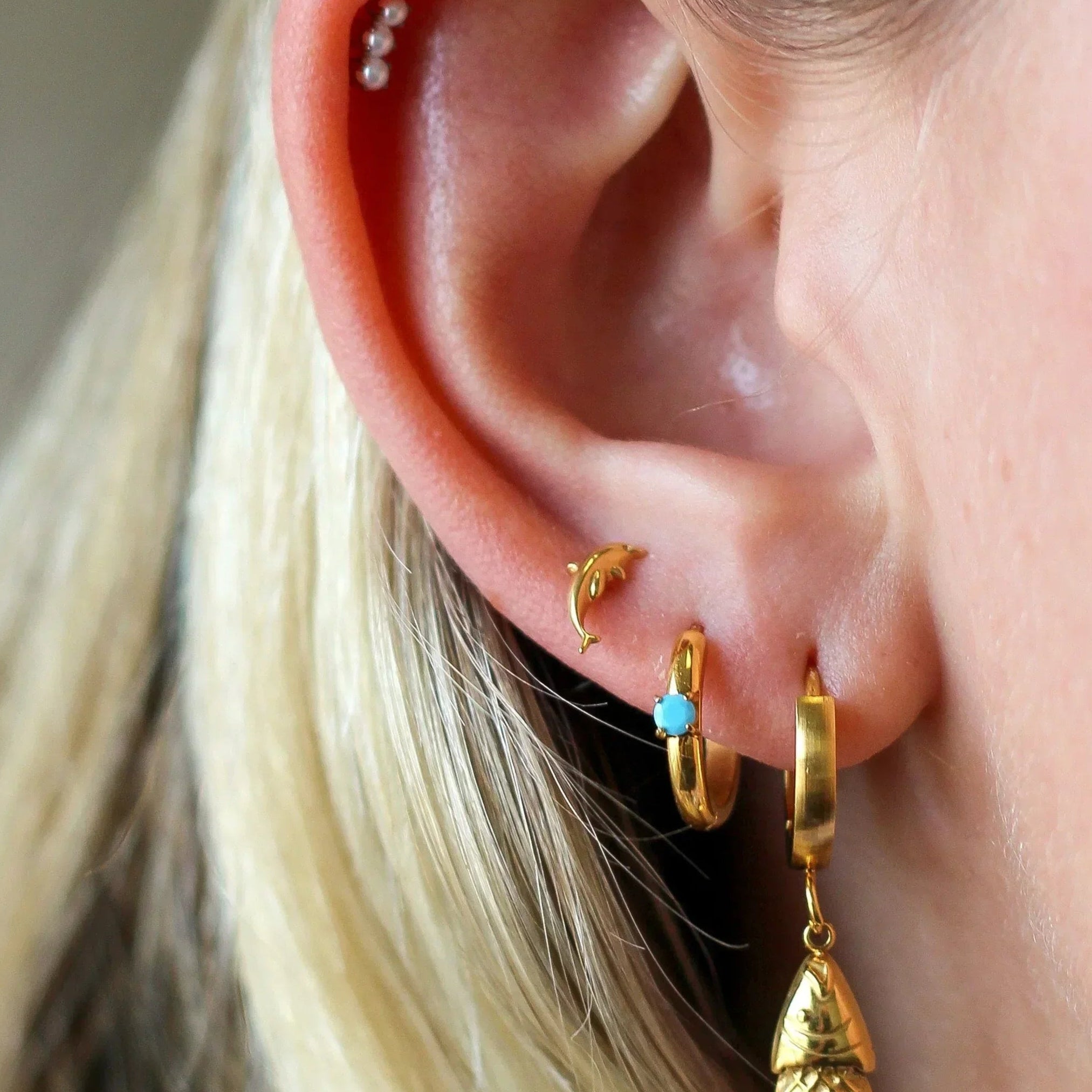 Close-up of an ear with gold earrings and a blurred background