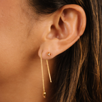 Close-up of an ear wearing a gold earring with a dark background
