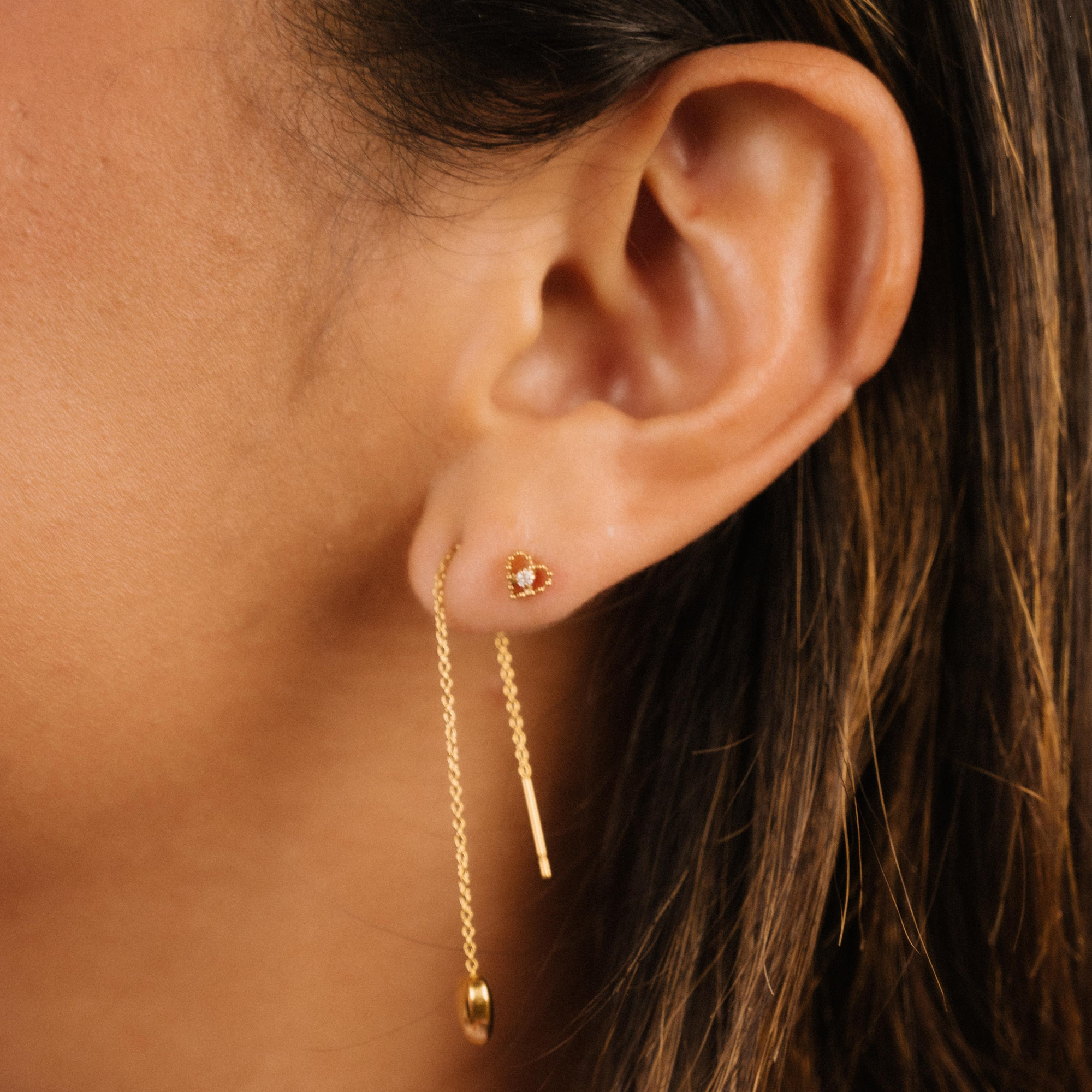 Close-up of an ear wearing a gold earring with a dark background